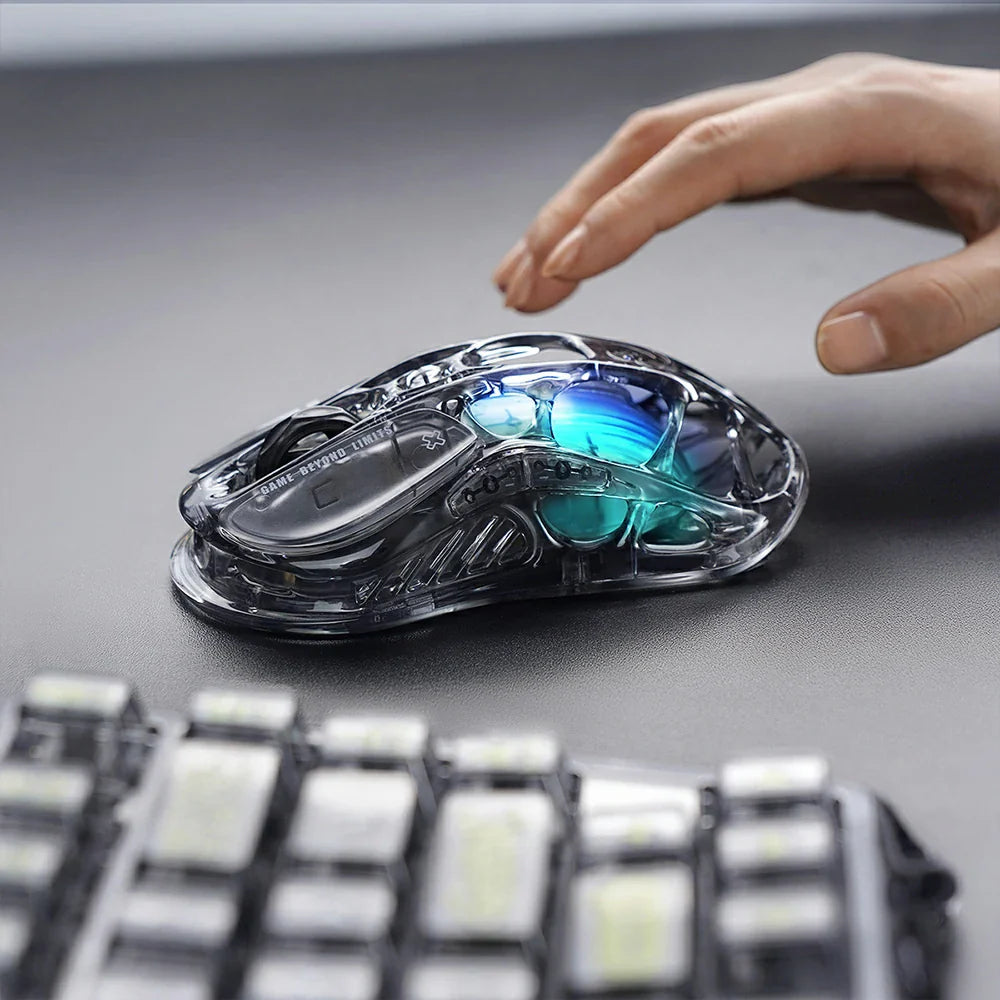 GravaStar Mercury M2 Transparent Black gaming mouse, a 2024 Red Dot Award-winning design featuring a sleek transparent black finish with ambidextrous ergonomic shape, compatible with palm, tip, and claw grips. Equipped with the high-precision PAW3395 sensor (26,000 DPI, 650 IPS acceleration, 1,000 Hz wireless polling rate) for pixel-perfect tracking, plus 82 hours of battery life (USB-C wired/Bluetooth 5.1). Highlighted specs: 5 programmable buttons with macro support, 5 customizable RGB lighting modes (16.