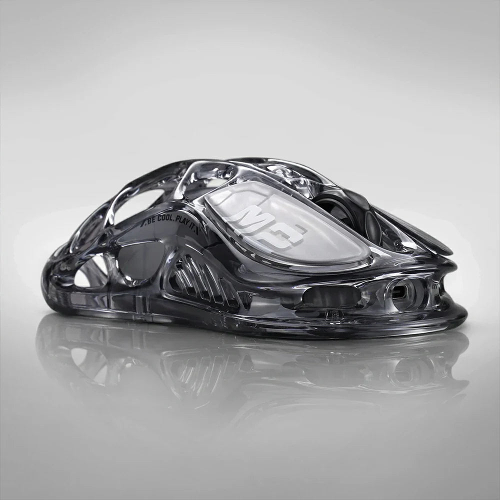 GravaStar Mercury M2 Transparent Black gaming mouse, a 2024 Red Dot Award-winning design featuring a sleek transparent black finish with ambidextrous ergonomic shape, compatible with palm, tip, and claw grips. Equipped with the high-precision PAW3395 sensor (26,000 DPI, 650 IPS acceleration, 1,000 Hz wireless polling rate) for pixel-perfect tracking, plus 82 hours of battery life (USB-C wired/Bluetooth 5.1). Highlighted specs: 5 programmable buttons with macro support, 5 customizable RGB lighting modes (16.